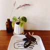 White tray with small items on a wooden surface, featuring a plant and decorative objects.